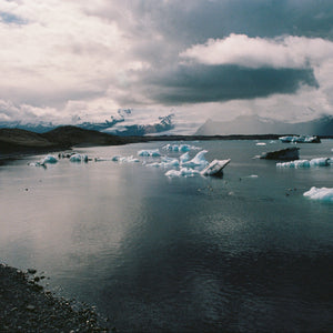 Glacier lagoon with icebergs and dark volcanic sand under a cloudy sky.