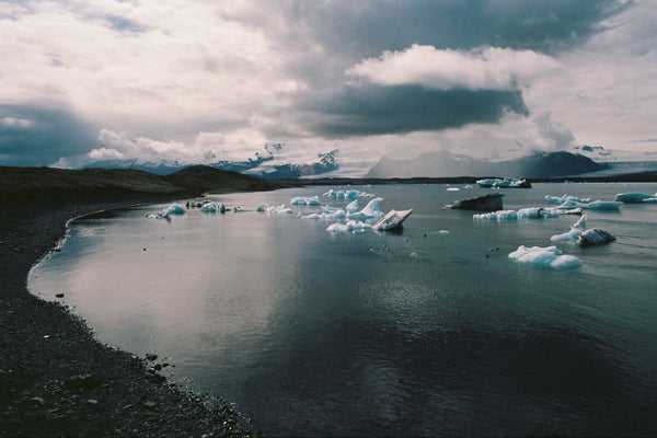 Glacier lagoon with icebergs and dark volcanic sand under a cloudy sky.