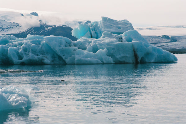 Large iceberg floating in a body of water with a mountainous landscape in the background.